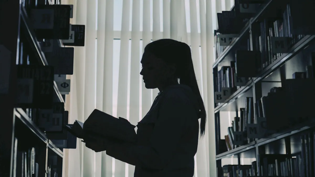 A silhouette of a college student opening a book in the library.