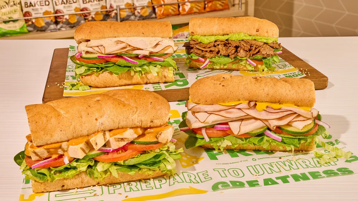 A collection of four different sandwiches on top of apper that has the Subway logo.