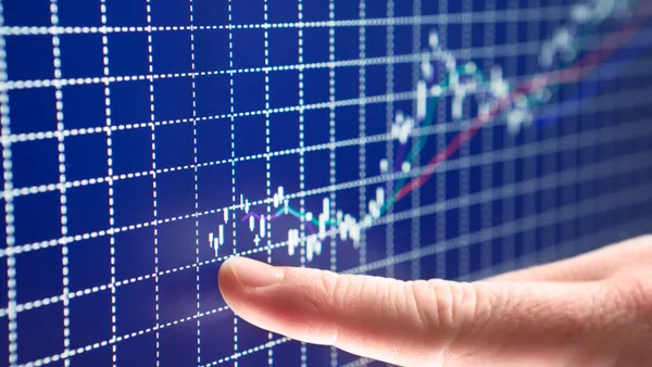 A person points to the start of a successful business on a blue stock market graph.