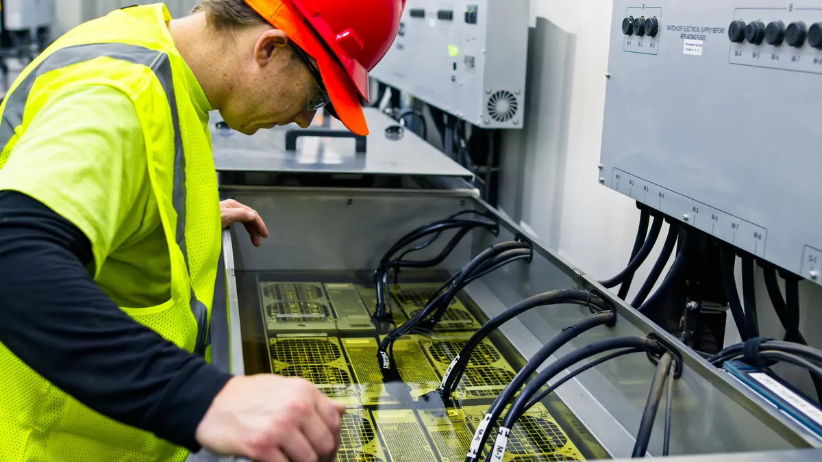 A man wearing a yellow safety vest and red hard hat working on equipment with tubes.