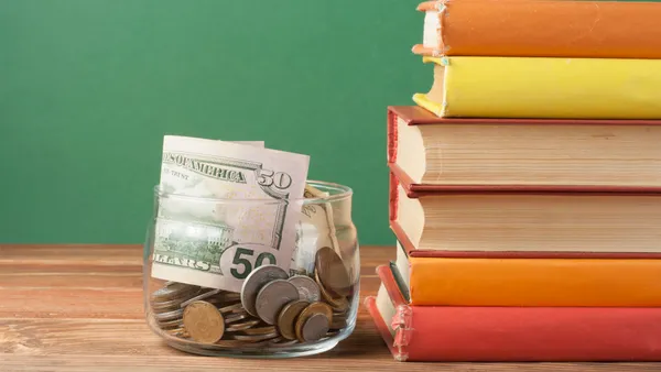 A jar of cash sits next to a stack of books on a teacher's desk.