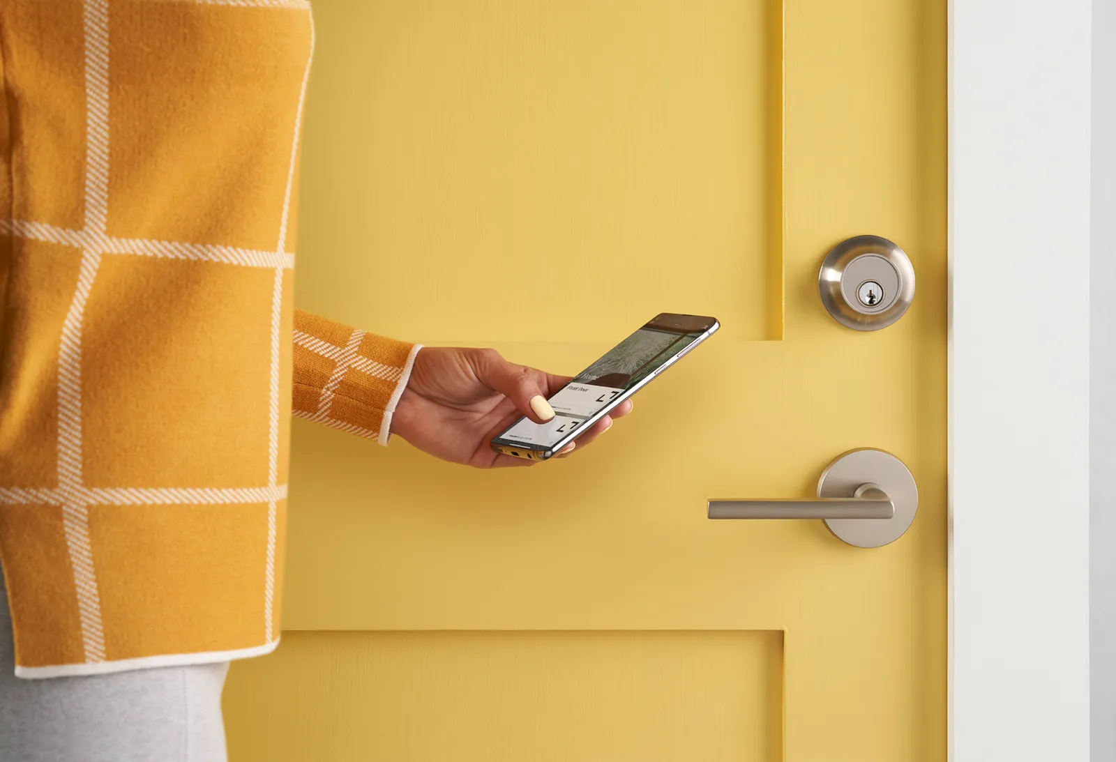 A person stands next to a yellow door, holding a phone.