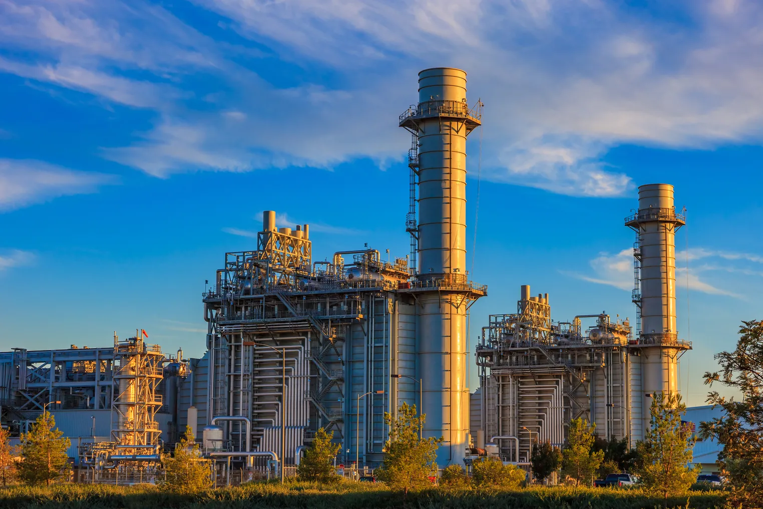 Natural gas fired turbine power plant with it's cooling towers rising into a cloud filled blue sky.