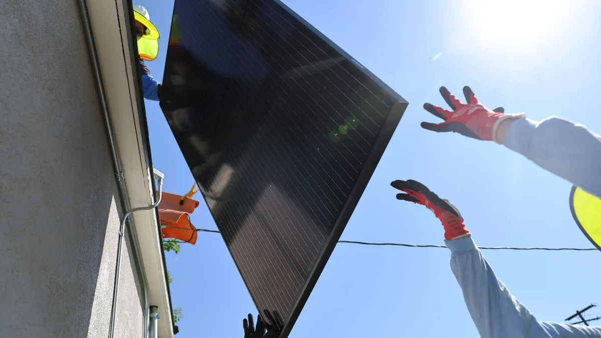 Workers hoist a solar panel on the rooftop of a home