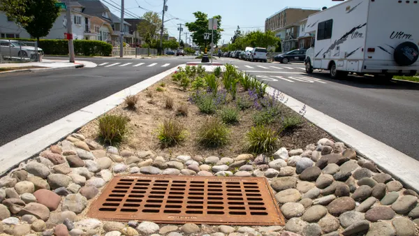 A strip in the middle of a city roadway with plants and a large grill over an opening.