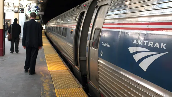 An Amtrak passenger train is stopped at Penn Station with passengers on the platform waiting to board.
