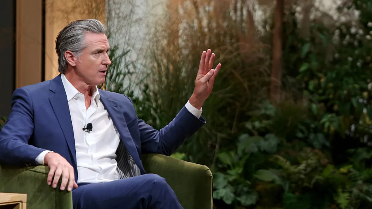 Gavin Newsom speaking on stage in business attire during a conference