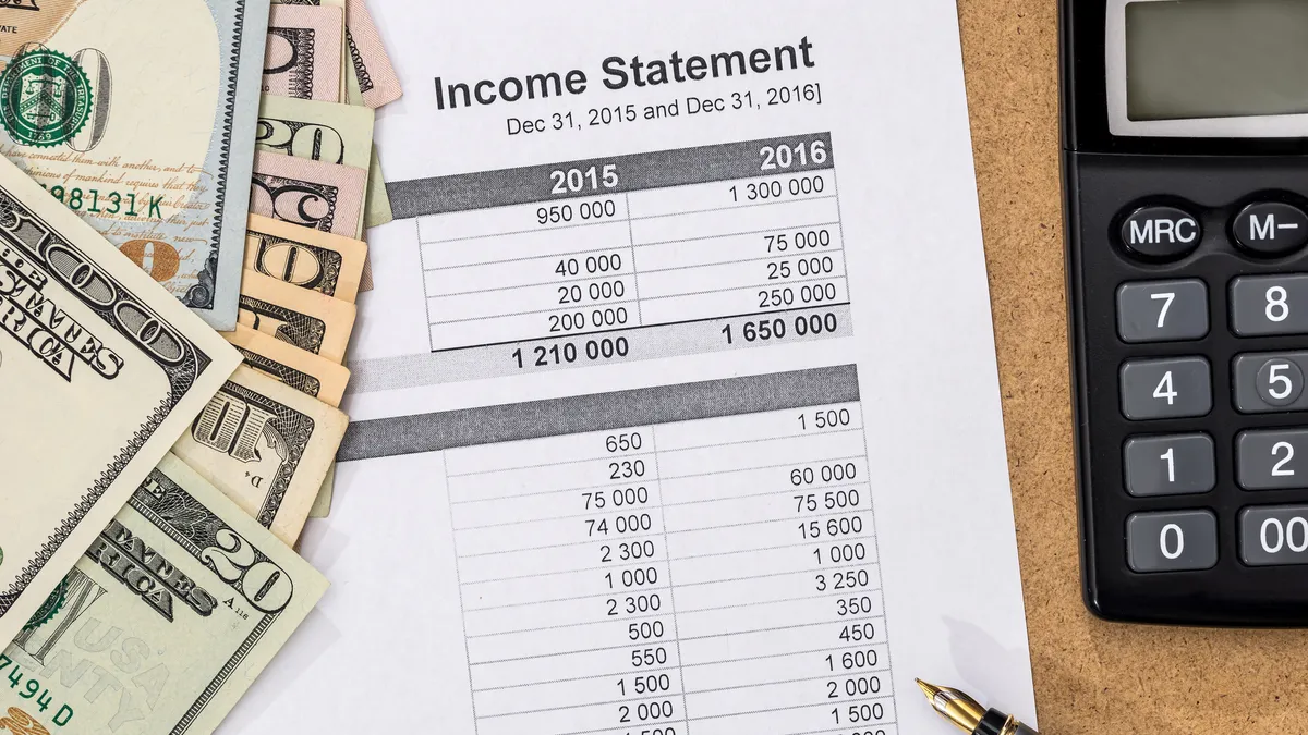 Photo of a paper income statement, calculator and several a two $100 bills and other cash.