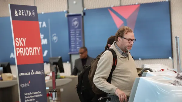 Travers check in for their flight at a kiosk in front of a Sky Priority sign.