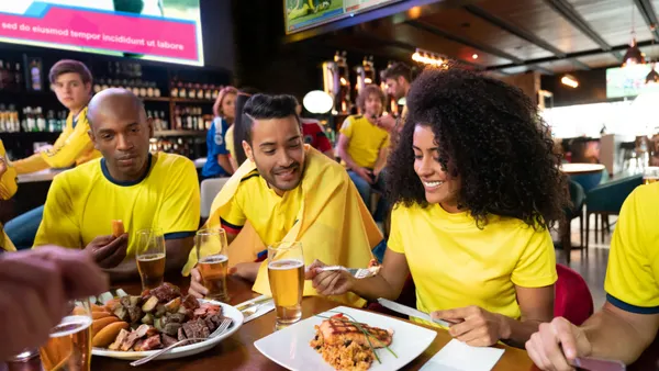 People dressed in yelp sit at a table inside a restaurant and bar eating food and drinking beer.