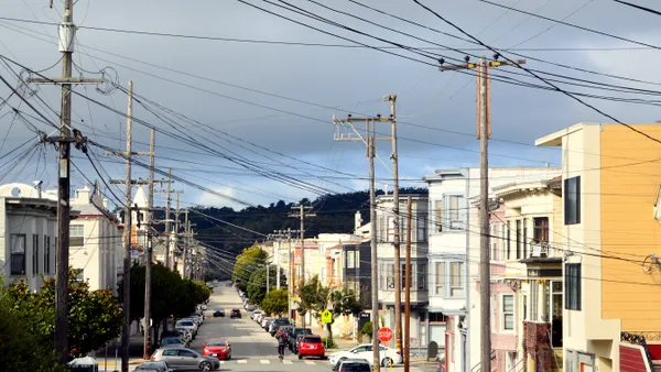 Looking down a city street lined with colorful houses, trees, cars and power lines.