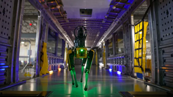 A black and yellow dog-like robot walking between two rail cars.