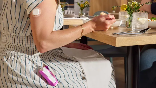 A person sits at a table with food, wearing a pink, rectangular device attached to a striped dress.