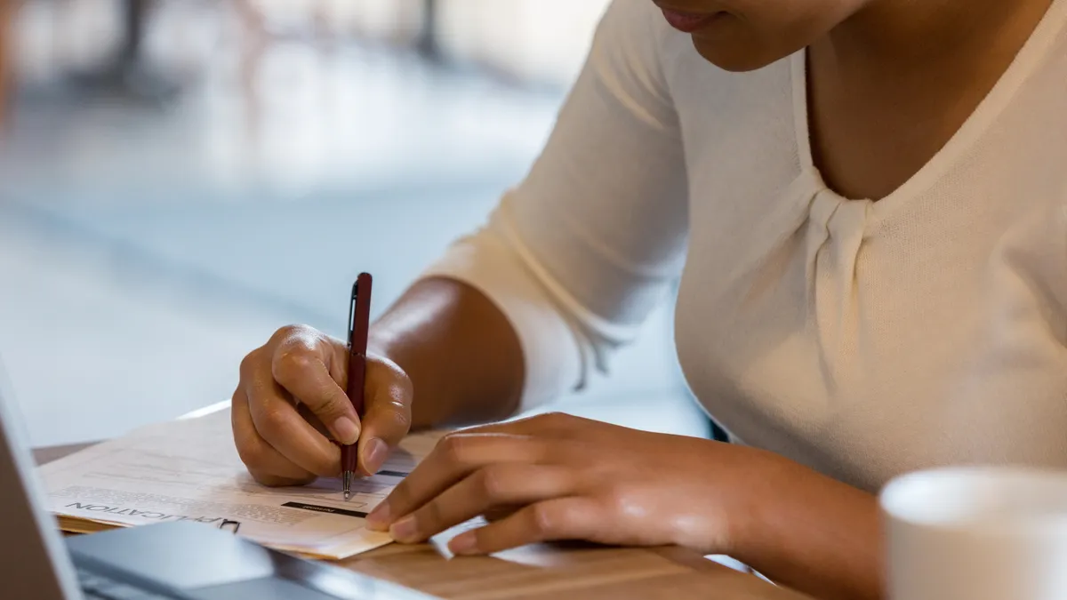 A woman references the information on her laptop to fill out a job application at the coffee shop.