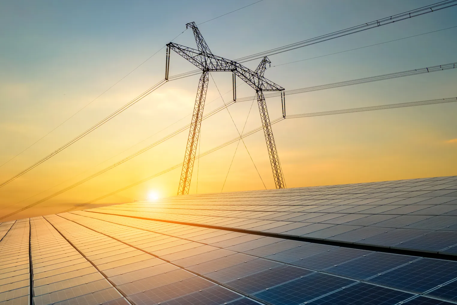 High voltage pylons with electric power lines transfering electricity from solar photovoltaic cells at sunrise.