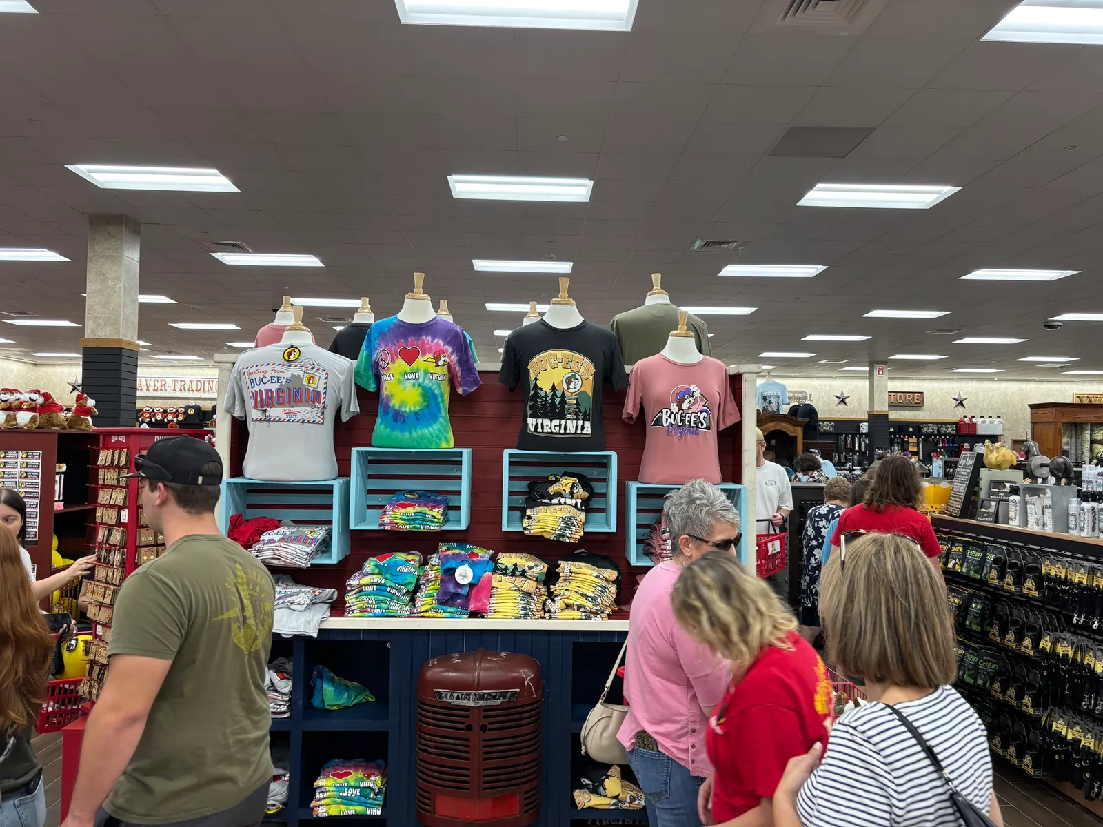 A photo of the interior of a large store. A display holds a variety of shirts in different designs, all of which say "Buc-ee's Virginia."