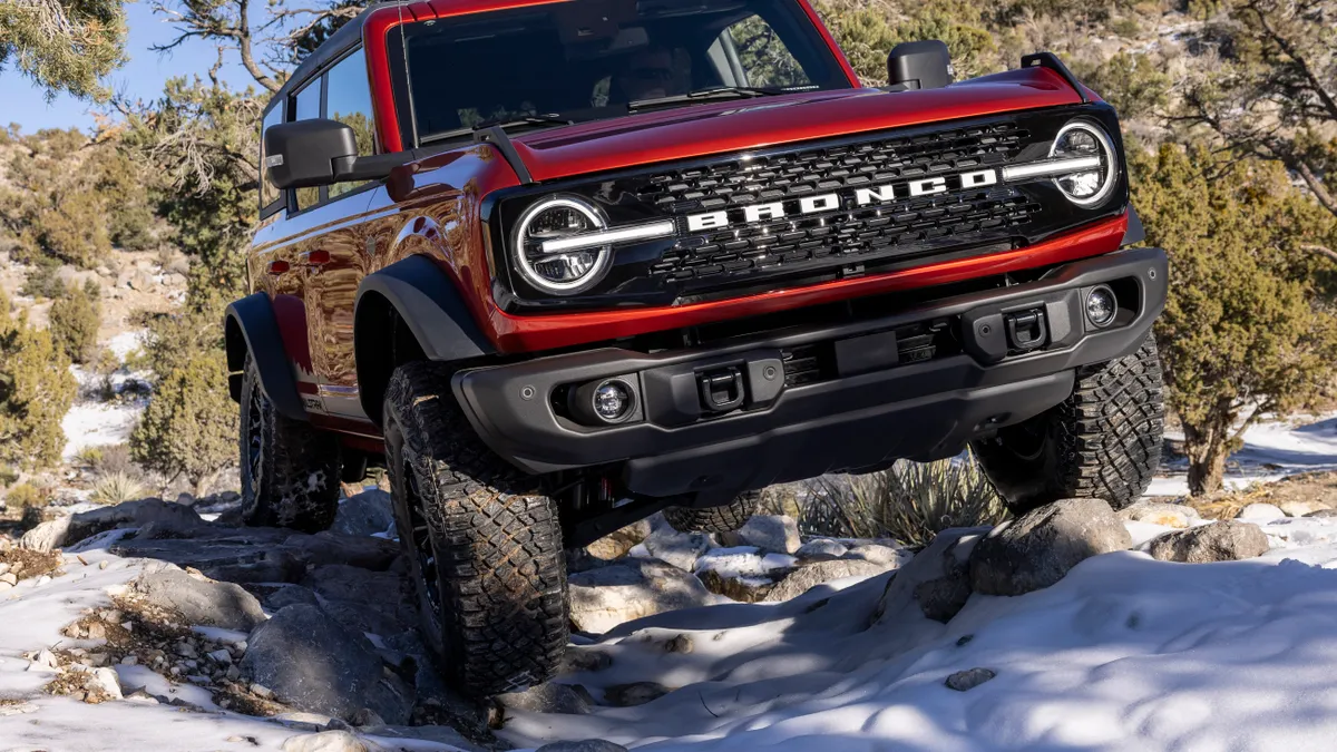 A red 2022 Ford Bronco traversing rocky terrain with snow visible on the ground.