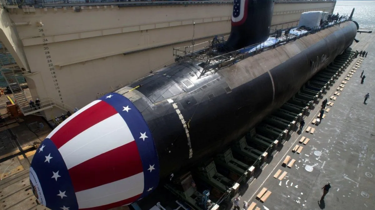 The USS John Warner in black, but tip is painted in red, white, and blue, laying on a fleet carrier under the sun.