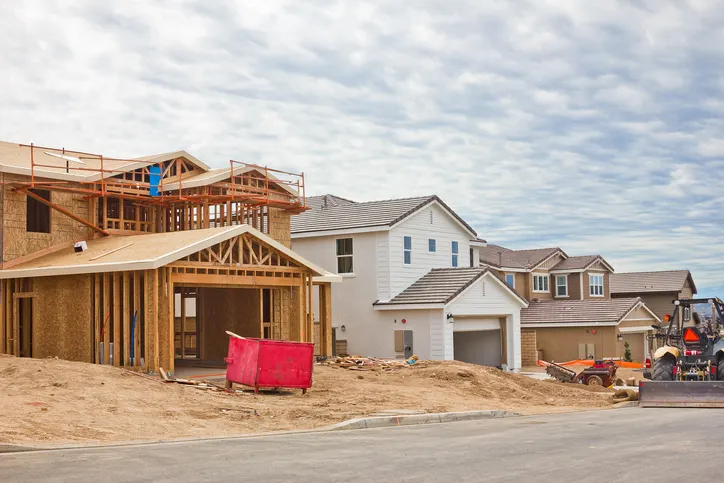 a wood frame on a new house next to two existing houses with a sand front yard
