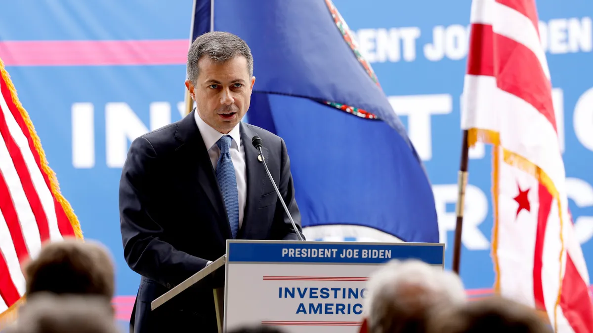 Man in suit and tie standing at podium with audience in the foreground.