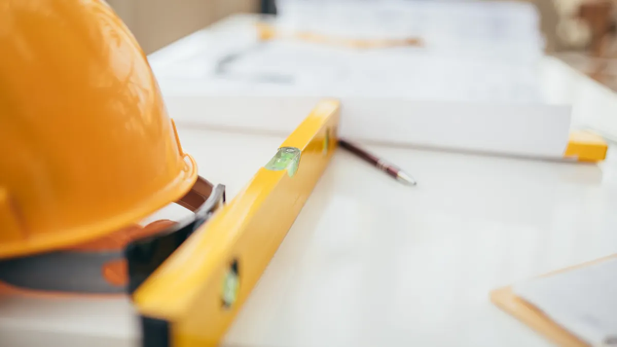 A photo of a hard hat, construction plans and tools on a table.