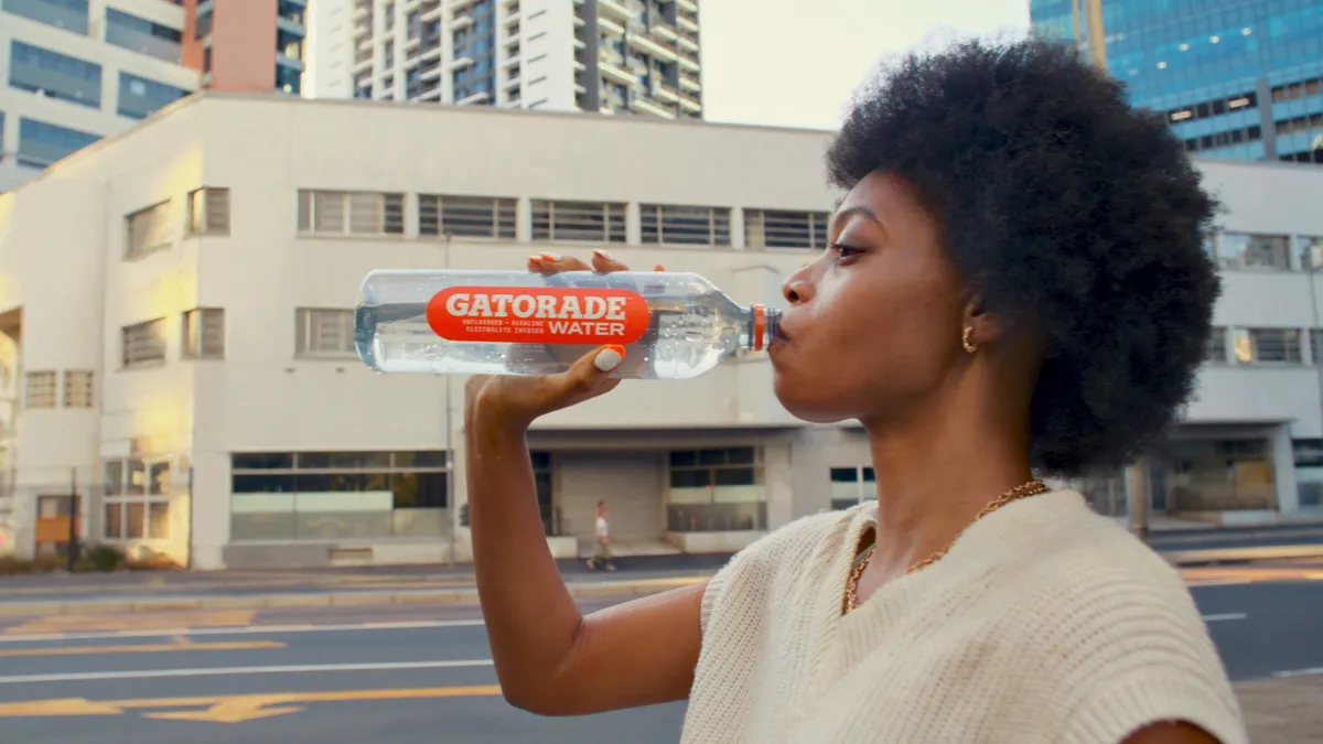 A women drinks from a Gatorade Water bottle while standing on a sidewalk.