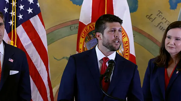 A man in a dark blue suit speaks behind a podium with the emblem of the U.S. Justice Department.