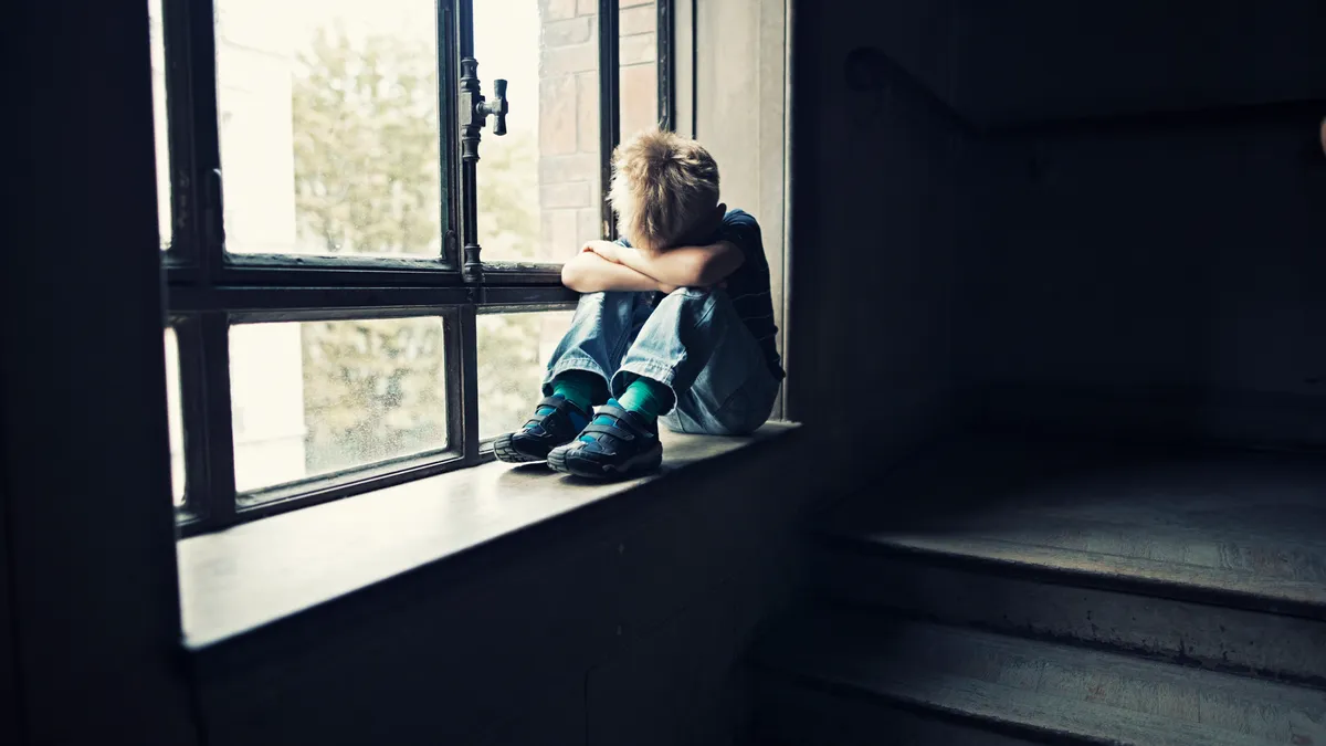 Sad child sitting on window in old staircase.