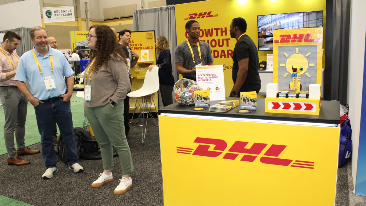 Multiple people stand inside a convention booth that has bright yellow walls with DHL branding.