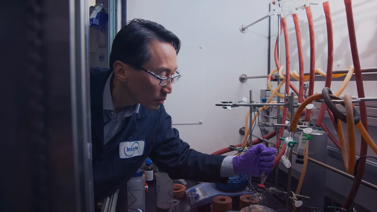A researcher, wearing a navy blue lab coat with the Incyte logo above a breast pocket, works in a research lab.