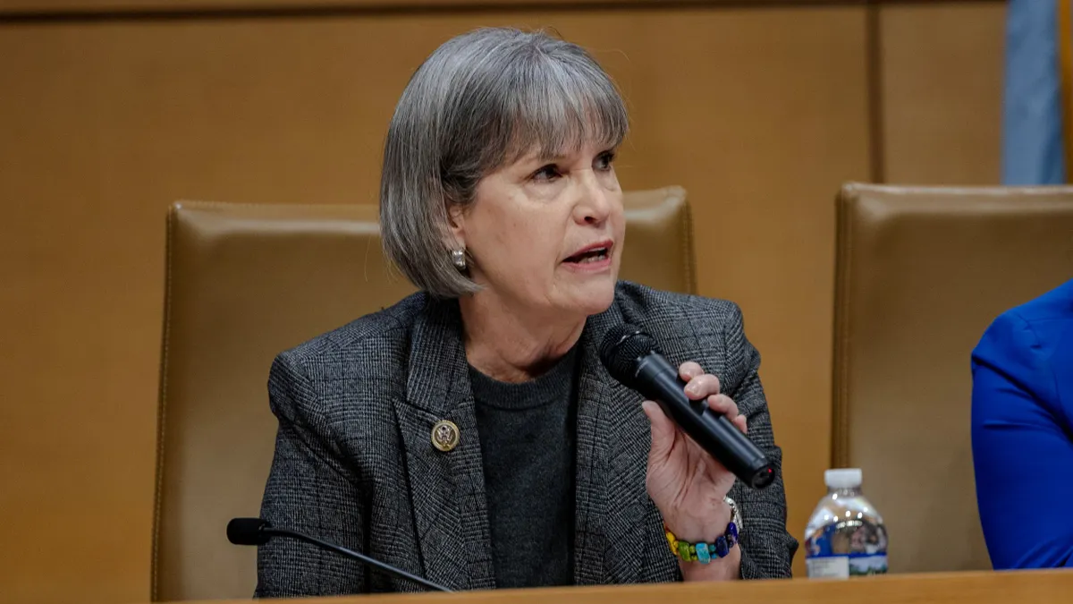 A woman with a gray bob hair do speaking into a mic.