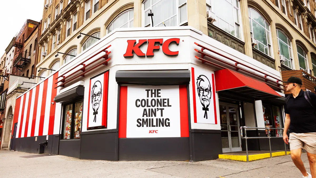 A pedestrian strolls by a KFC ad that shows Colonel Sanders scowling.