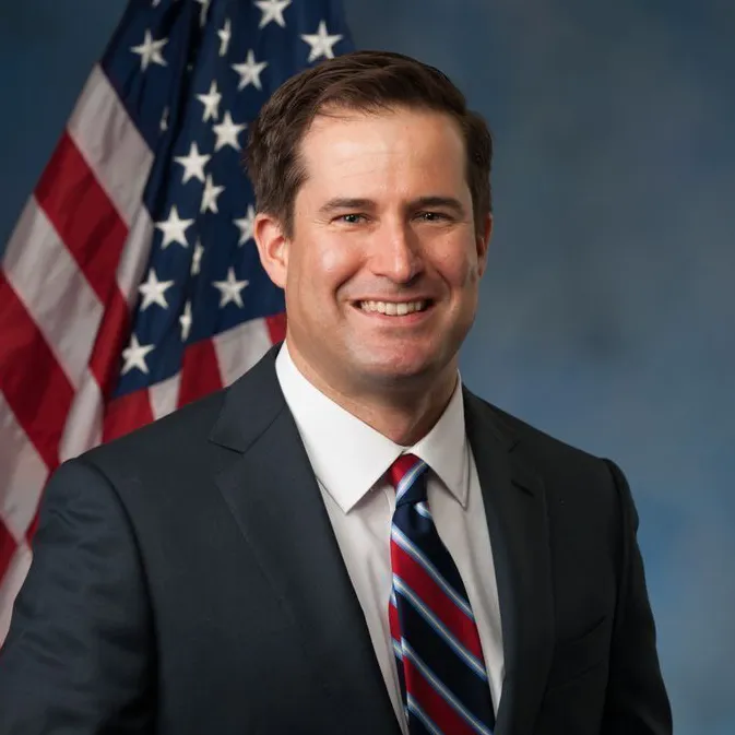 A portrait photo of U.S. Representative Seth Moulton, a Massachusetts Democrat, standing in front of the American flag.