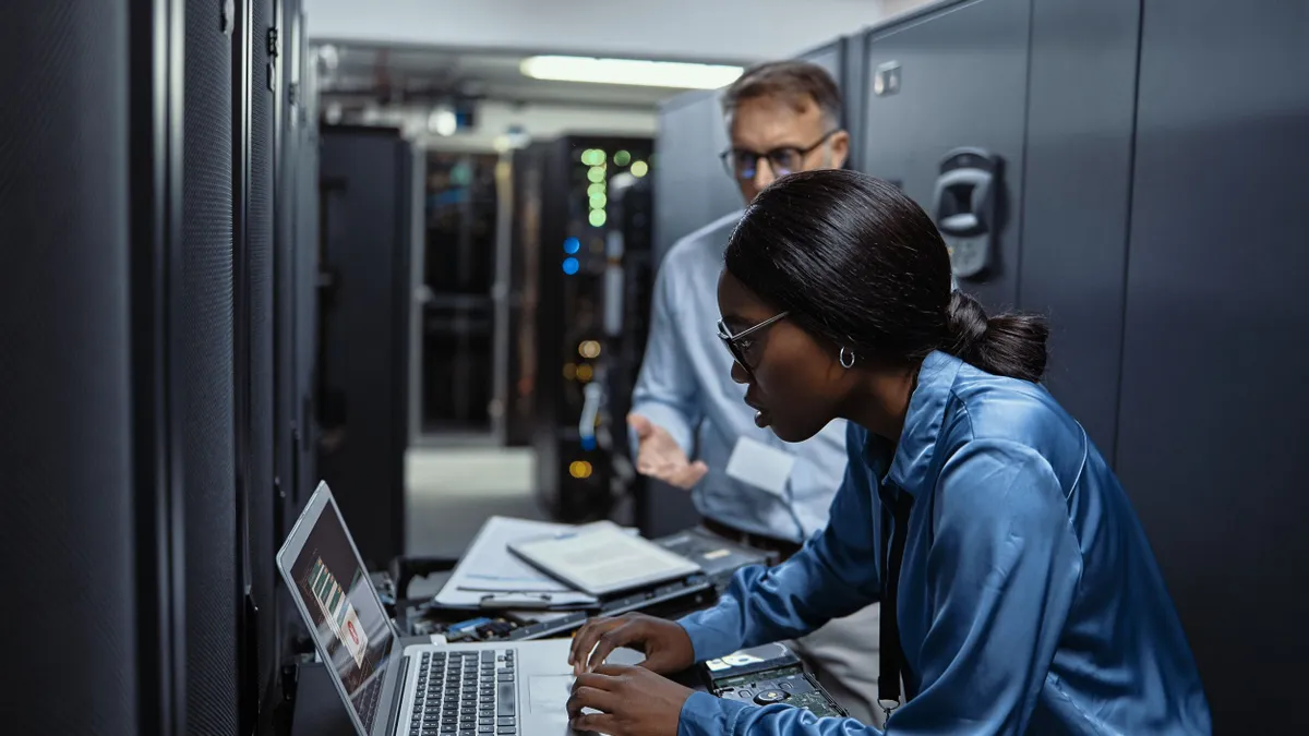 Two IT technicians using a laptop in a server room.