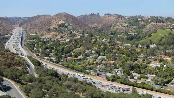 Aerial view of congested multilane highway between hills and homes.