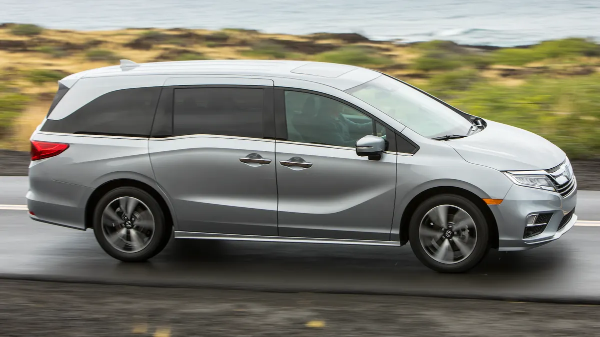 A silver 2020 Honda Odyssey minivan driving on a road with a body of water in the background.