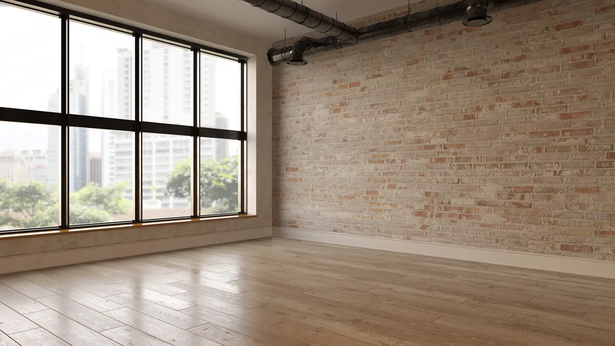 An empty room with brick walls, large windows and exposed pipes on the ceiling.