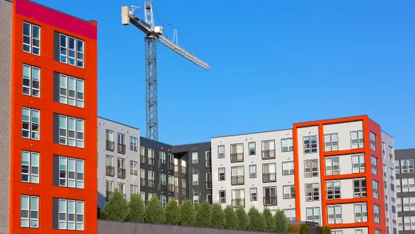 A modern residential building in red and silver stands prominently, with a crane towering behind it.