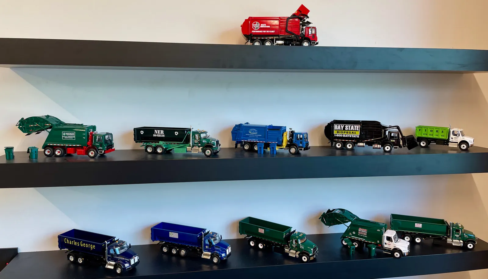 Shelves displaying miniature replicas of 11 different waste collection trucks