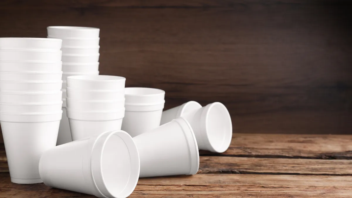 A stack of white styrofoam cups on a brown wooden table.