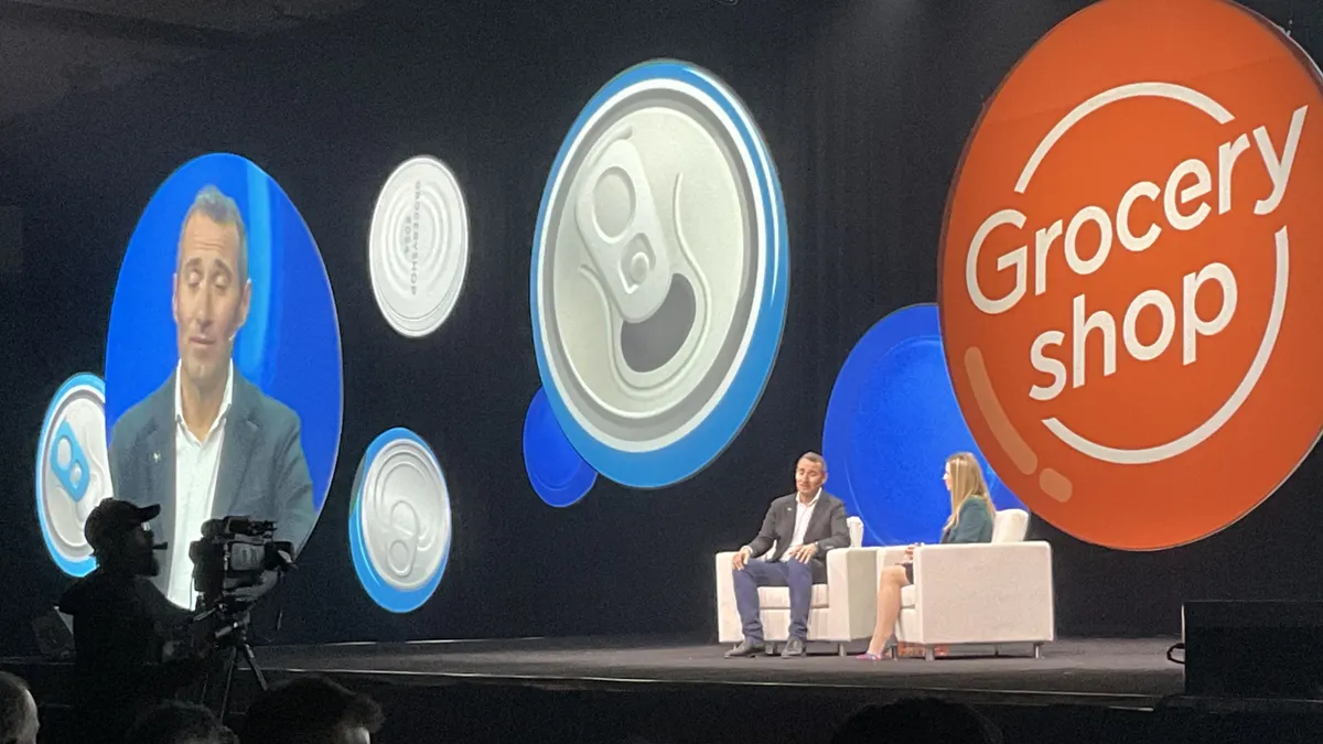 Two people sitting in white chairs in front of circular signs on a stage