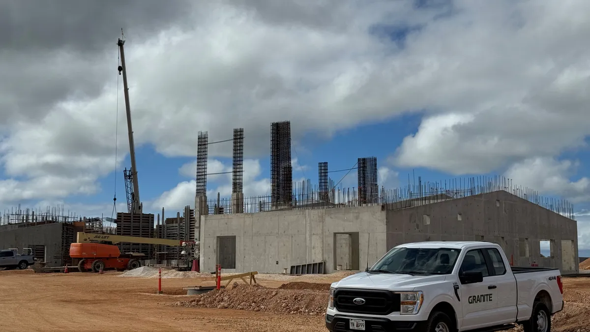 A truck is parked in front of a partially complete concrete structure in a dirt parking lot.