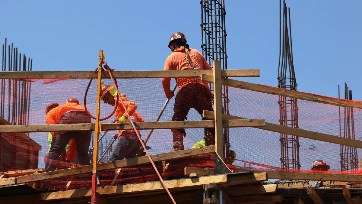 Construction workers are on a platform. The platform is also under construction, and workers wear safety gear.