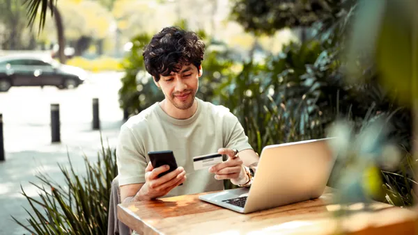 Man sitting at table outside with card in one hand and a phone in another hand.