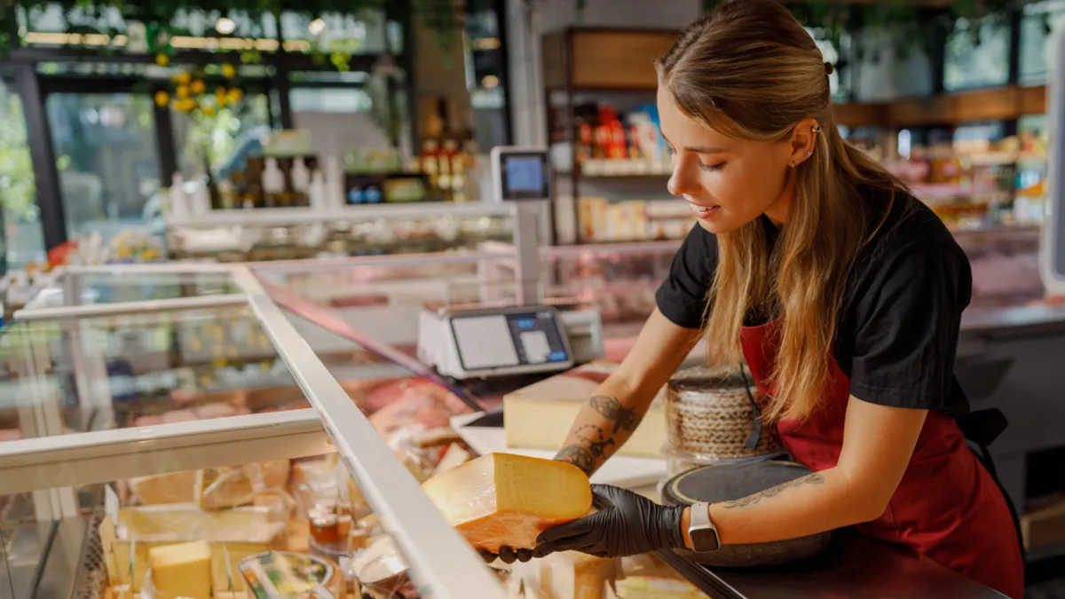A deli employee lifting a cheese wheel