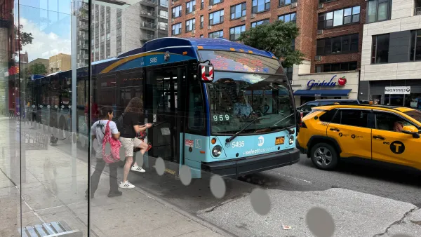 People board a bus at a with a yellow taxi driving by.