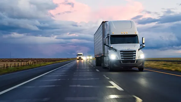 A semi-truck and other traffic with headlights on driving on an interstate on a stormy evening.