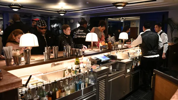 Guests gather around a bar as bartenders mix drinks.