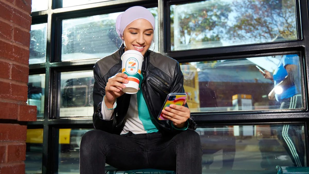 A photo of a person drinking 7-Eleven coffee and looking at their phone.