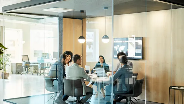 Business colleagues sitting at conference table seen through glass wall. Multi-ethnic coworkers are discussing in board room at office. They are planning strategy.